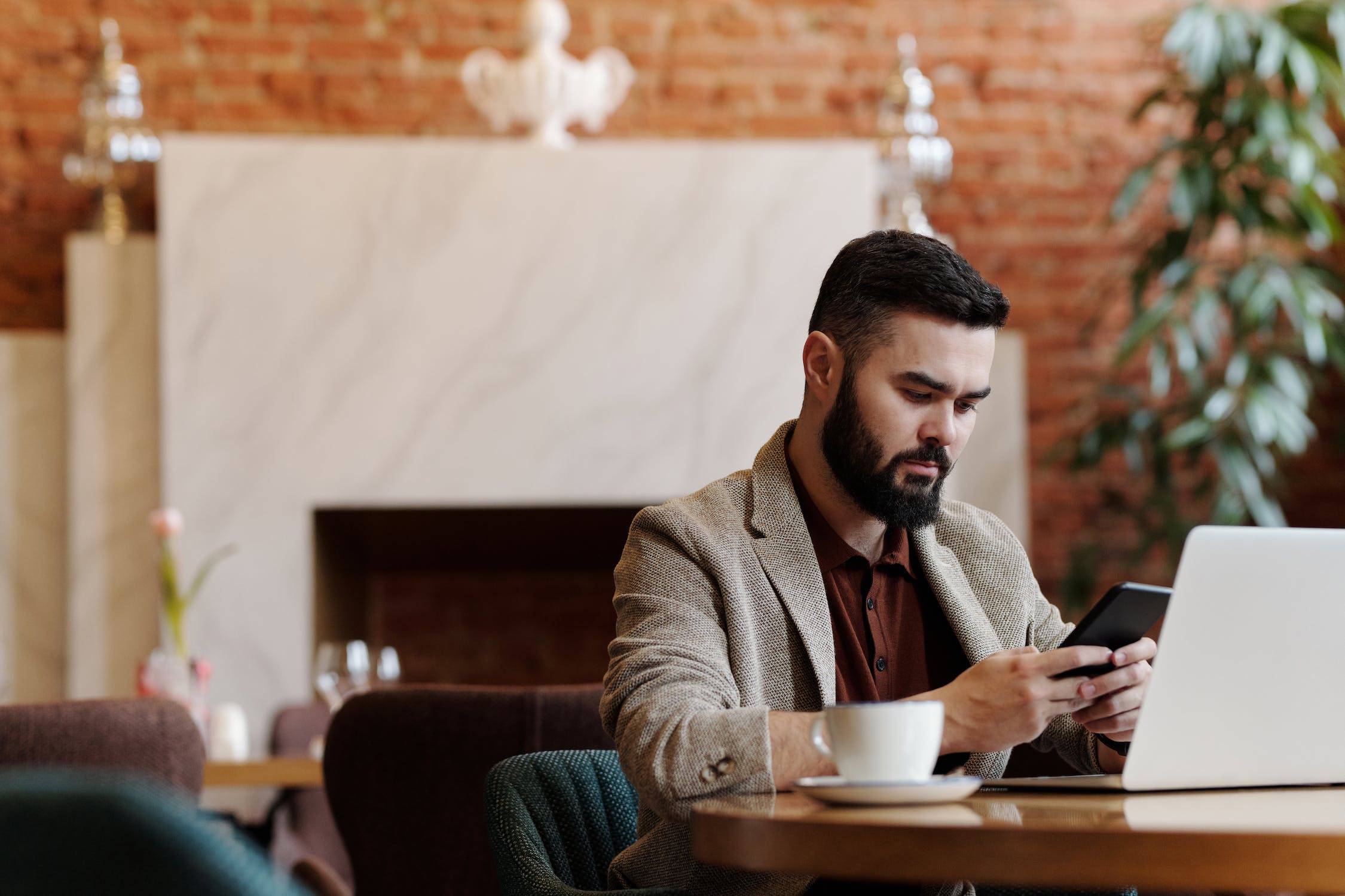 Man at a table with laptop in front of him looking a this phone