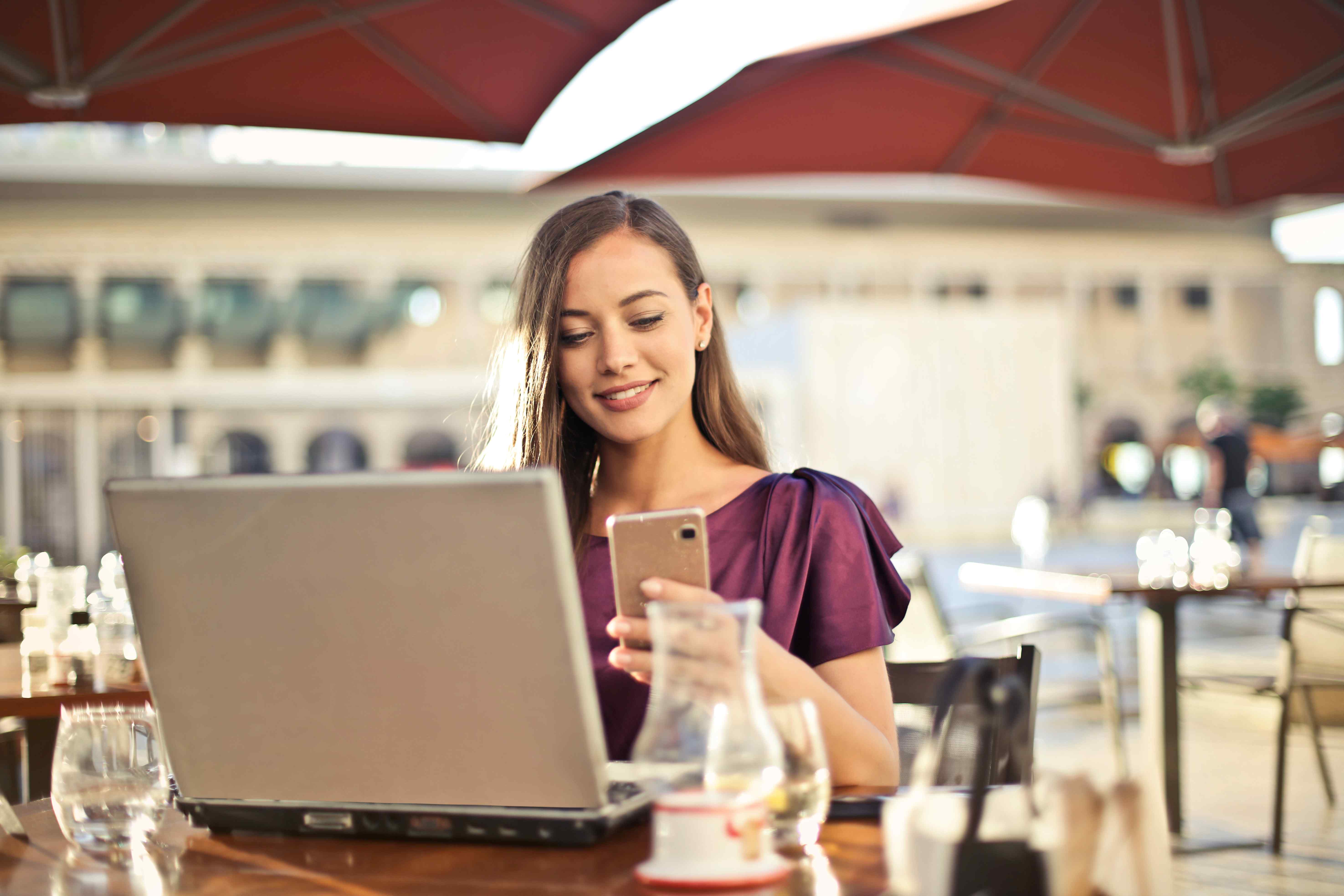 Woman sitting at a cafe with her laptop checking her phone notifications